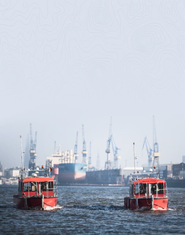 Zwei rote Boote auf See mit größeren Schiffen im Hintergrund